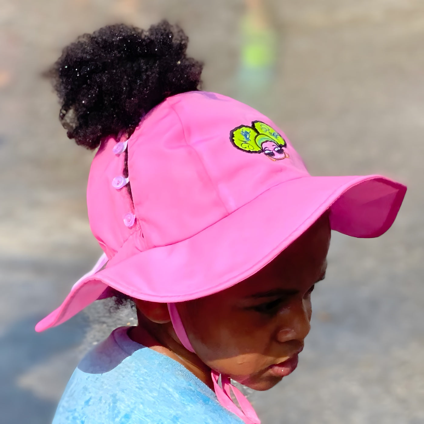 A kid wearing the pink hat with their ponytail puff flowing through the snap-button back opening