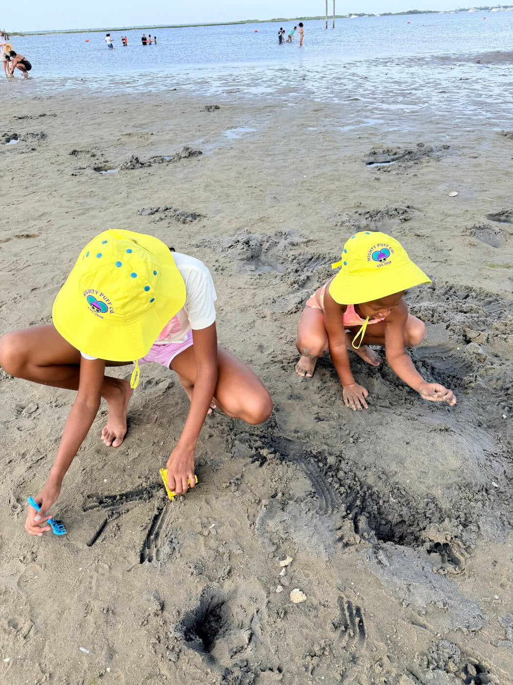 Two kids in Lemon Lime Mighty Puff hats digging in the sand at the beach