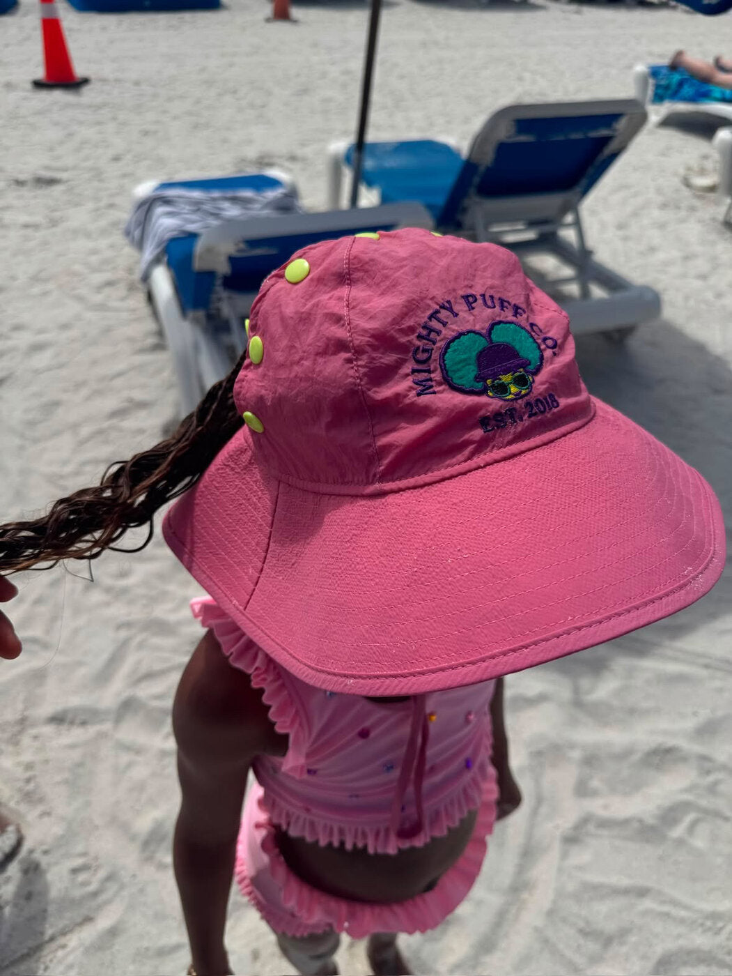 Beach day — braids flowing under the pink Mighty Puff Hat
