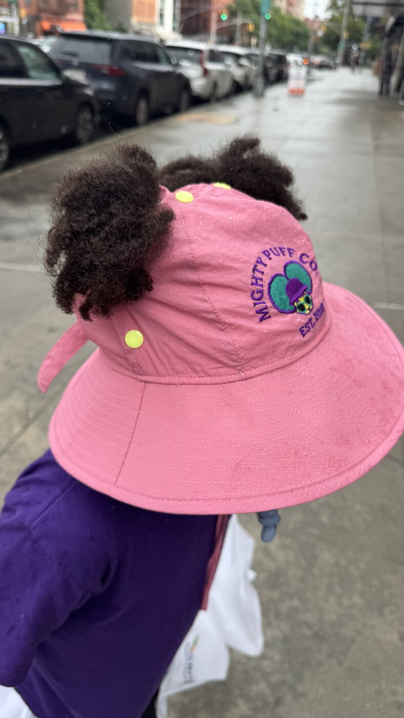 Puffs flowing out the back of the pink hat on a rainy city walk