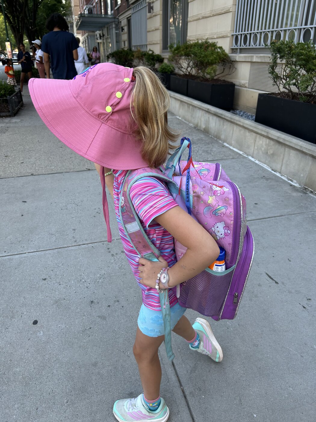 Ponytail flowing over the pink hat brim on the walk to school
